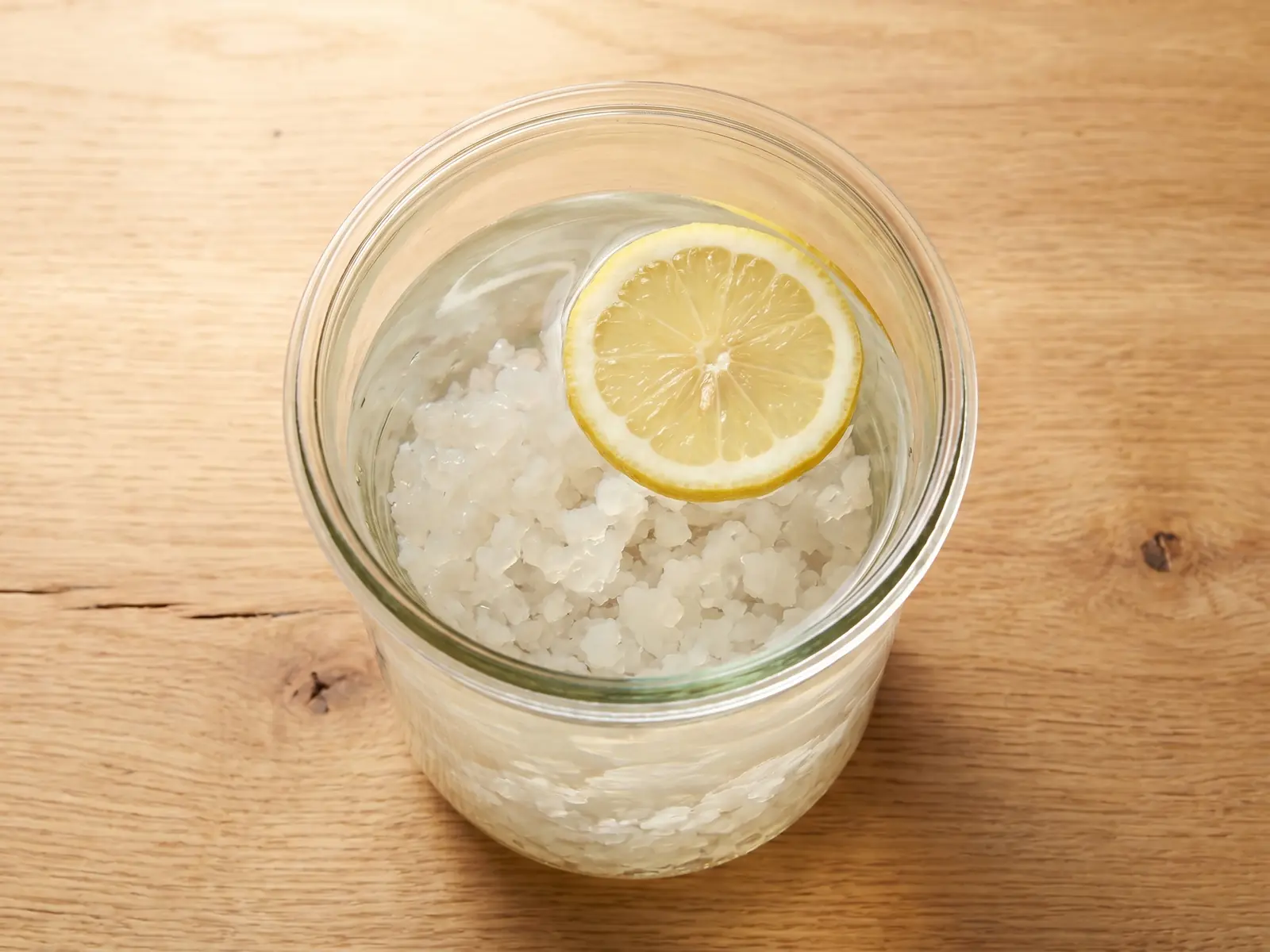 Wasserkefir im Glas von oben mit hellen Kristallen im Wasser und einer Zitronenscheibe an der Oberfl&auml;che.