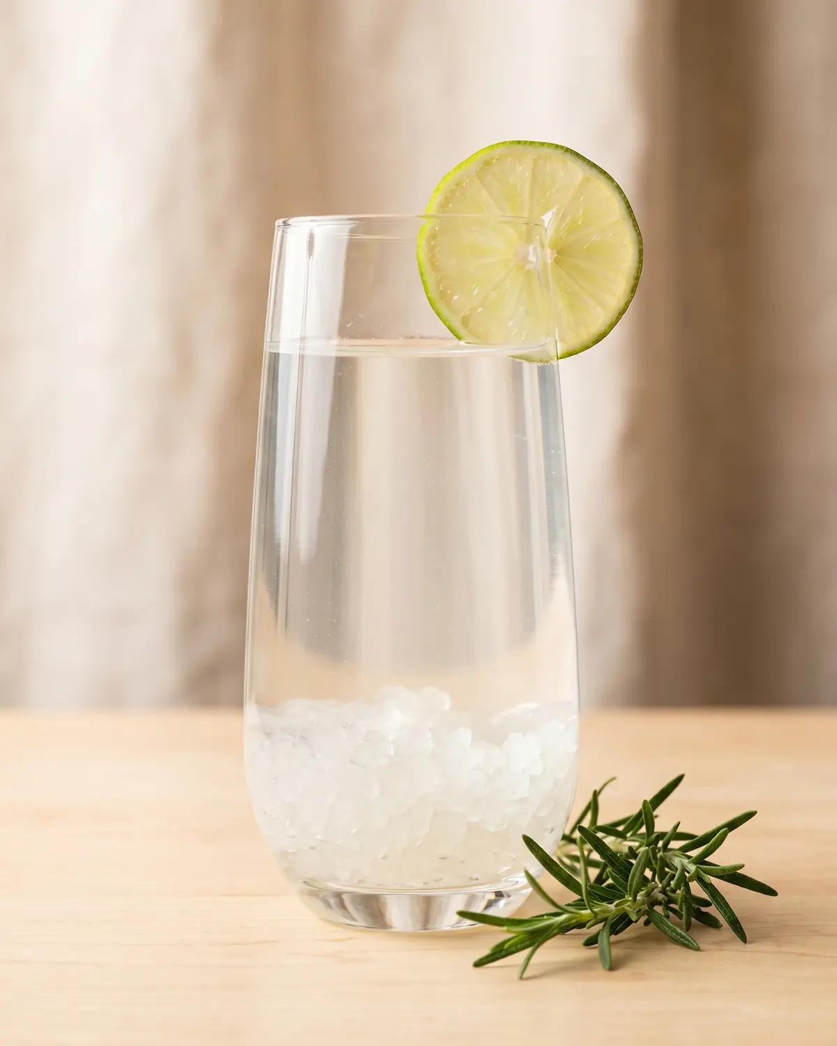 wasserkefir für anfänger Ein Glas Wasserkefir mit Limettenscheibe, frischem Rosmarin und hellem Licht von oben auf der Oberfläche