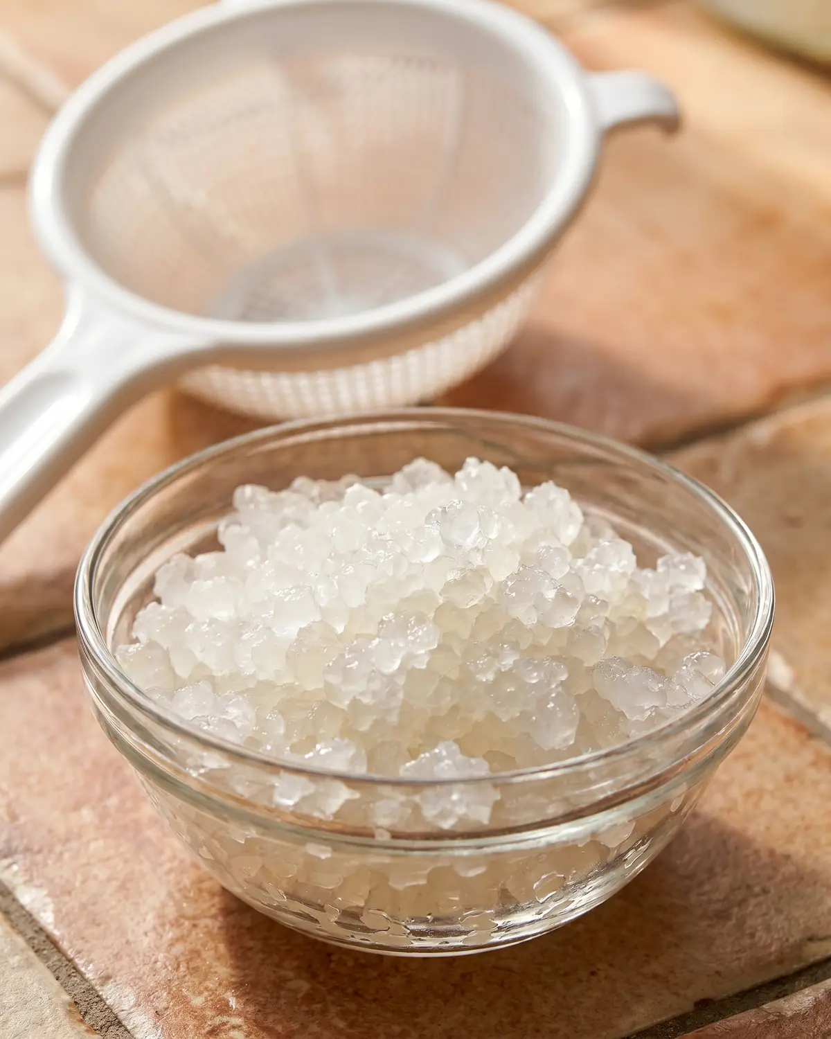 wasserkefir kristalle werden kleiner Kleine helle Wasserkefir-Körnchen in einer Schale, im Hintergrund liegt ein weißes Sieb.