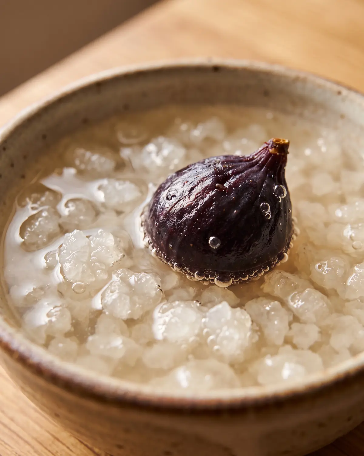 Nahaufnahme einer rehydrierten Trockenfeige &uuml;ber Wasserkefir-Kristallen mit feinen Bl&auml;schen im Glas
