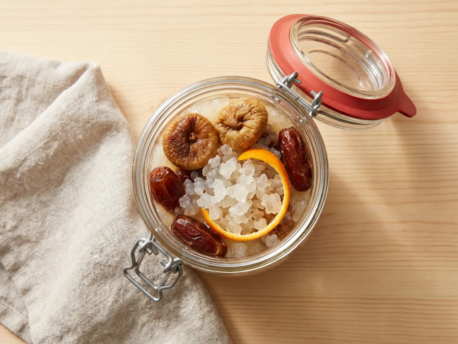 Glas mit Wasserkefir in der Zweitfermentation, Feigen, Datteln und Orangenschale auf heller Fl&auml;che
