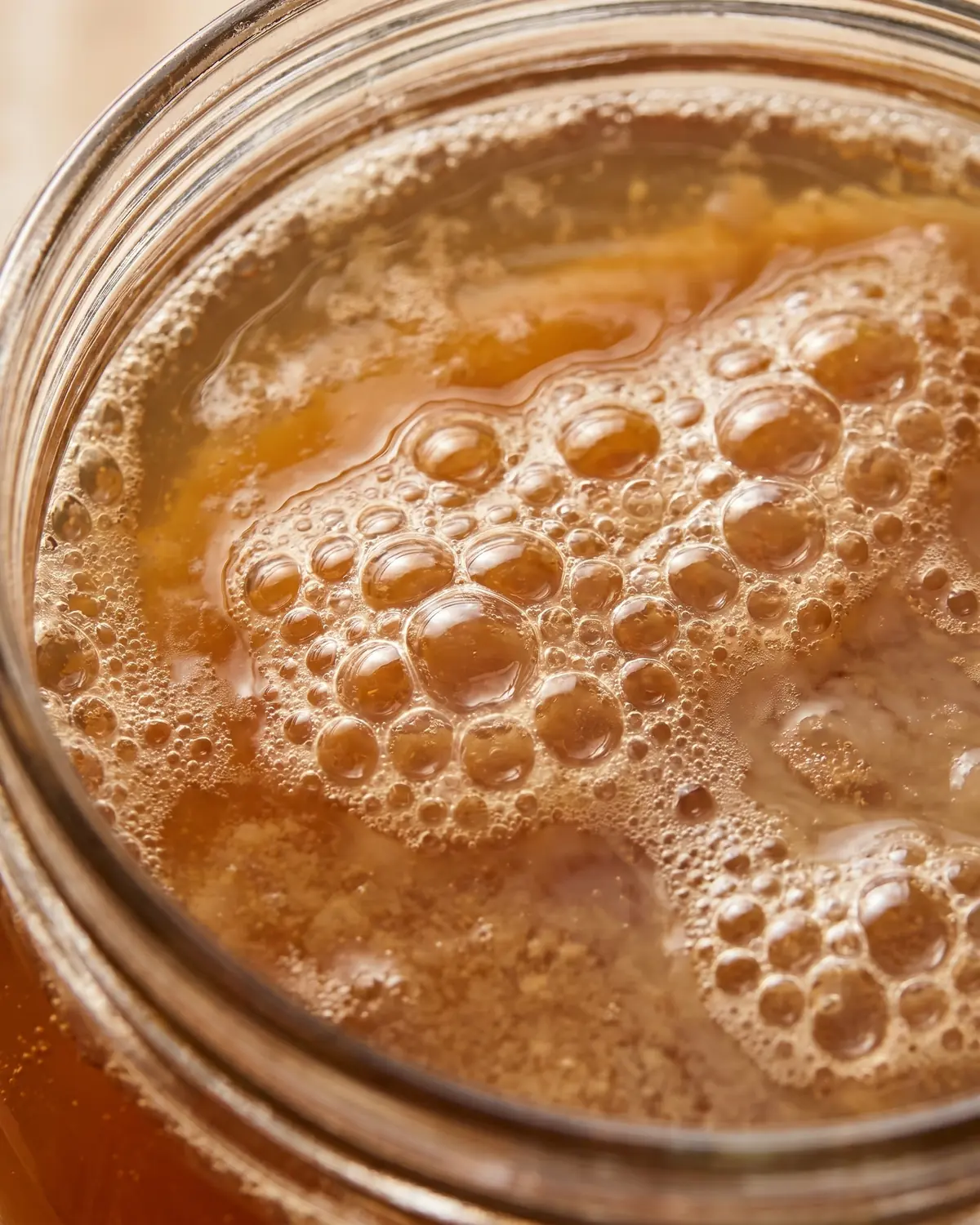 Nahaufnahme von feinen Bl&auml;schen auf bernsteinfarbenem Kombucha in einem angeschnittenen Glas.